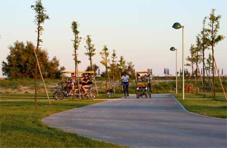 Persone su veicoli a pedali percorrono un sentiero circondato da alberi in un parco.