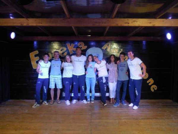 Un gruppo di persone in posa su un palco di legno con una scritta colorata sullo sfondo.