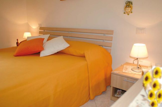 Un letto matrimoniale con copriletto arancione e cuscini su un comodino con lampada.