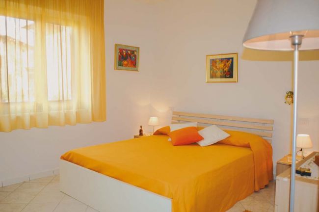 Stanza luminosa con un letto matrimoniale arancione e tende coordinate, quadri alle pareti.