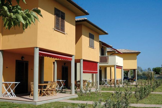 Villette con terrazze, sedie e tavoli sotto tende rosse su prati verdi.