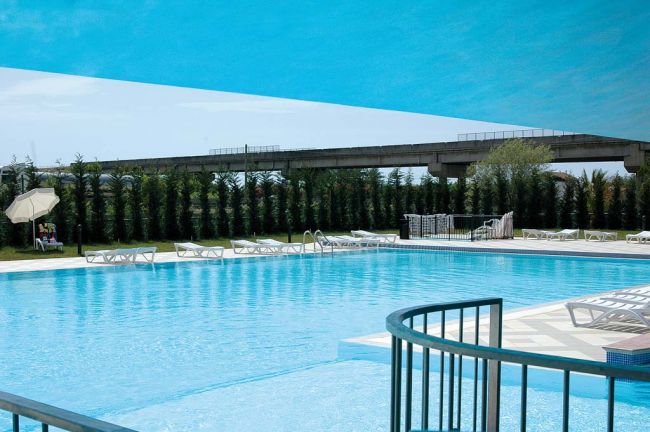 Grande piscina all'aperto circondata da lettini e ombrelloni.