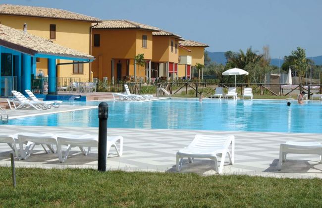Piscina all'aperto con lettini bianchi e villette colorate sullo sfondo.