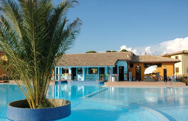 Piscina con palma centrale, vista su edificio azzurro e villette.