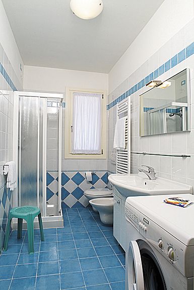 Bagno con piastrelle blu, doccia, lavatrice e servizi igienici.