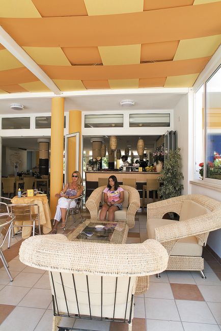 Due persone sedute in un'area lounge con divani intrecciati e soffitto a strisce arancioni.