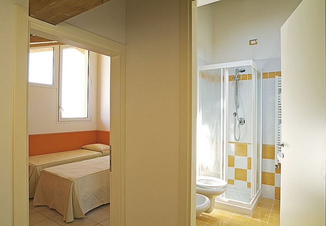 Camera da letto e bagno con doccia, divisi da un corridoio.