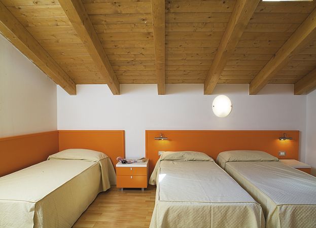 Tre letti singoli con testiere arancioni in una stanza con soffitto in legno.