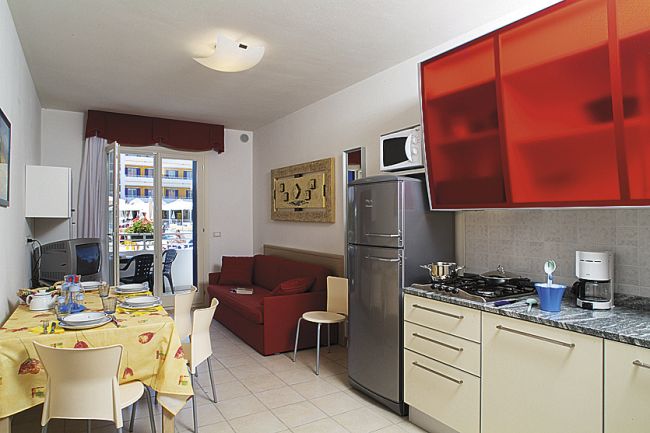 Cucina abitabile con tavolo apparecchiato, divano rosso e terrazzo.