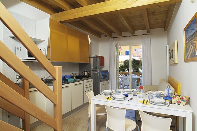 Cucina e zona pranzo con soffitto in legno e porta finestra su terrazzo.