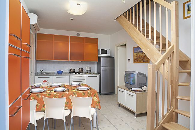 Cucina moderna con arredi arancioni, tavolo apparecchiato e scala in legno.