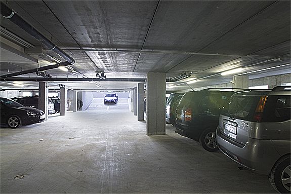 Parcheggio sotterraneo con auto parcheggiate e uscita in lontananza.