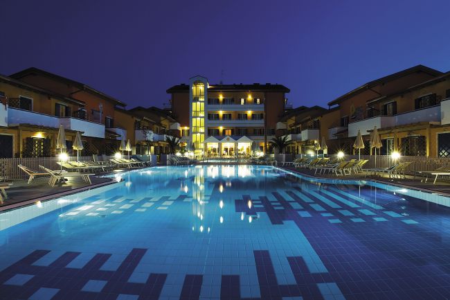 Piscina illuminata di sera davanti a un grande edificio con balconi.