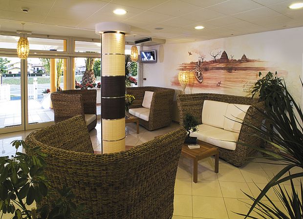 Area salotto con divani di vimini e cuscini bianchi, pianta in primo piano.