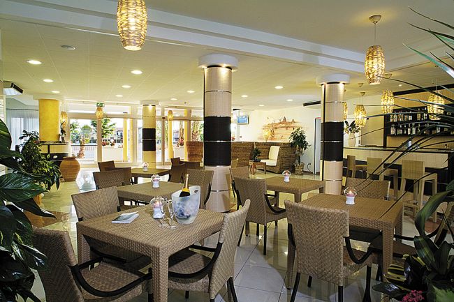 Sala da pranzo con tavoli e sedie di vimini, bottiglia di vino su un tavolo.