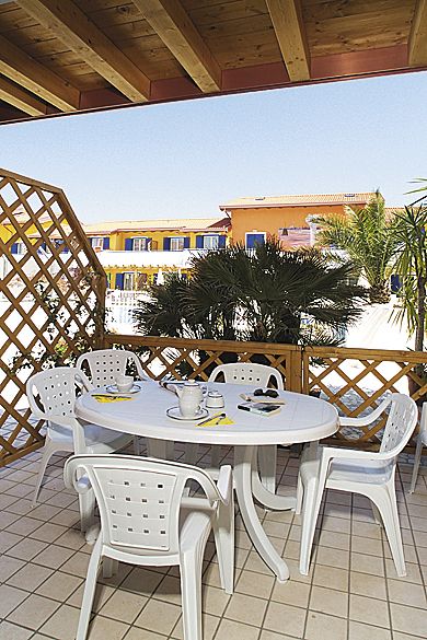 Tavolo rotondo bianco con sedie su un patio, palme e edifici sullo sfondo.
