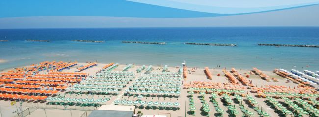 Ombrelloni colorati disposti ordinatamente su una spiaggia sabbiosa vista mare.