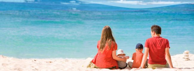 Famiglia in spiaggia seduta sulla sabbia, di fronte al mare azzurro.
