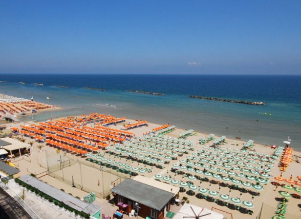 Spiaggia con ombrelloni arancioni e verdi disposti in file ordinate, mare azzurro sullo sfondo.