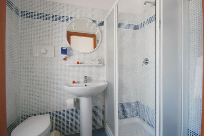 Un bagno con doccia, lavabo, specchio rotondo e piastrelle a mosaico blu e bianche.