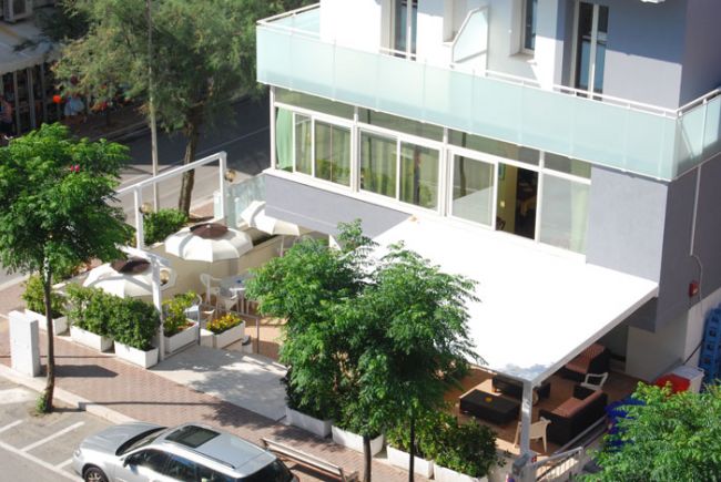 Terrazza esterna di un edificio moderno con sedie e tavoli, parzialmente coperta.