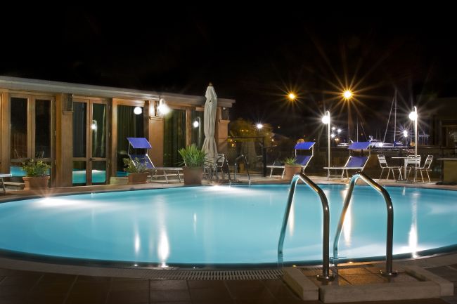 Piscina illuminata di notte con sedie a sdraio.