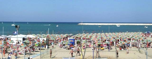 Spiaggia gremita di ombrelloni colorati e mare sullo sfondo.