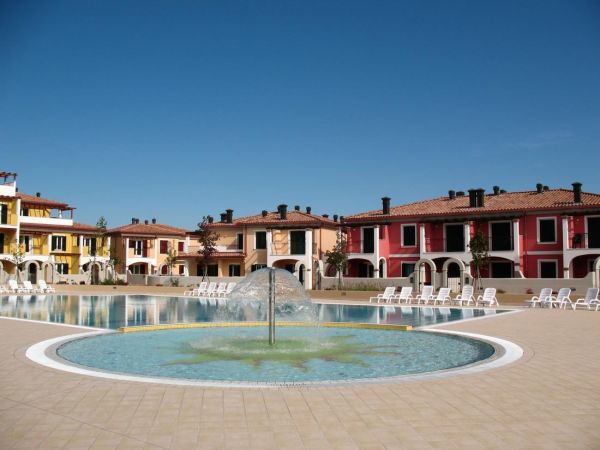 Piscina circolare con sdraio, case colorate sullo sfondo.