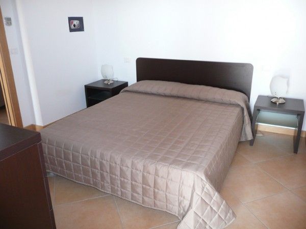 Stanza da letto con letto matrimoniale coperto da trapunta marrone e due comodini con lampade.