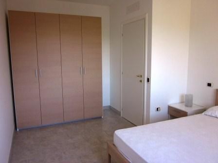 Una stanza con armadio a sei ante, letto accanto a un comodino, pavimento in piastrelle.