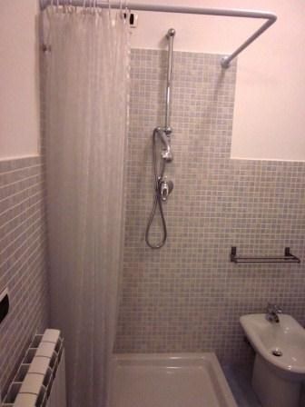 Doccia con tenda trasparente e soffione, piastrelle grigie, appendi asciugamani.
