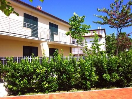 Una casa a due piani con balconi, circondata da un giardino verde e un cielo blu.