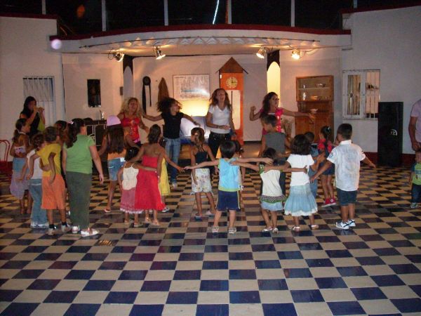 Bambini e adulti in cerchio su pavimento a scacchi.