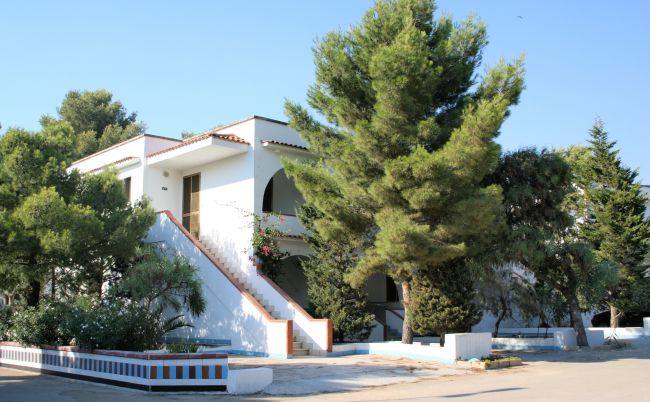 Edificio bianco a due piani con una scala esterna, alberi intorno.