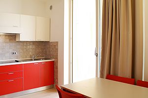 Cucina moderna con mobili rossi, tavolo con sedie rosse, tenda beige.