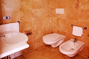 Bagno rivestito in piastrelle beige con lavabo, WC e bidet.