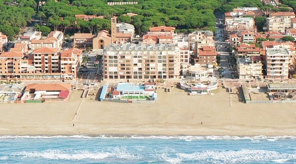 Vista aerea di una spiaggia con edifici residenziali e vegetazione sullo sfondo.