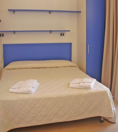 Camera con letto matrimoniale, copriletto chiaro e asciugamani piegati. Pareti e arredi in blu.