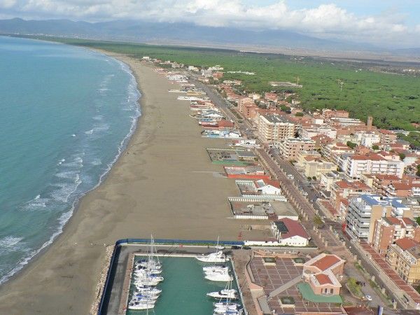 Vista aerea di una spiaggia ampia con edifici e un piccolo porto turistico lungo la costa.