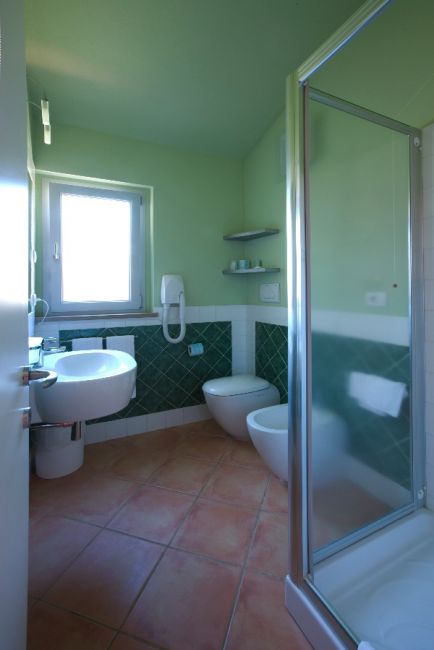 Un bagno verde con doccia, lavabo e bidet, dotato di finestra e piastrelle verdi.