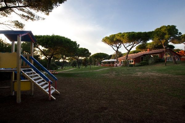 Area giochi e giardino con alberi, cielo sereno.