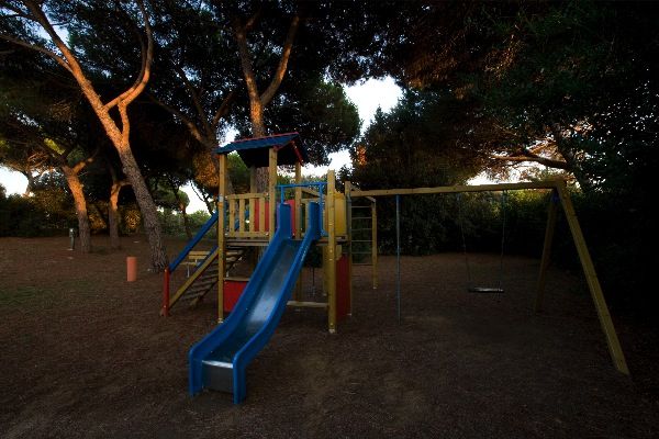 Scivolo blu e altalene in un parco giochi ombreggiato.