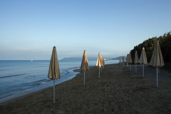 Ombrelloni chiusi su una spiaggia sabbiosa al tramonto.
