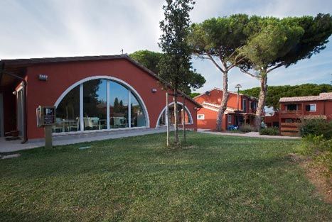 Edificio rosso con grandi finestre ad arco, circondato da alberi.
