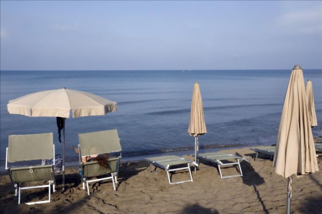 Due lettini con ombrelloni su una spiaggia sabbiosa di fronte al mare calmo.
