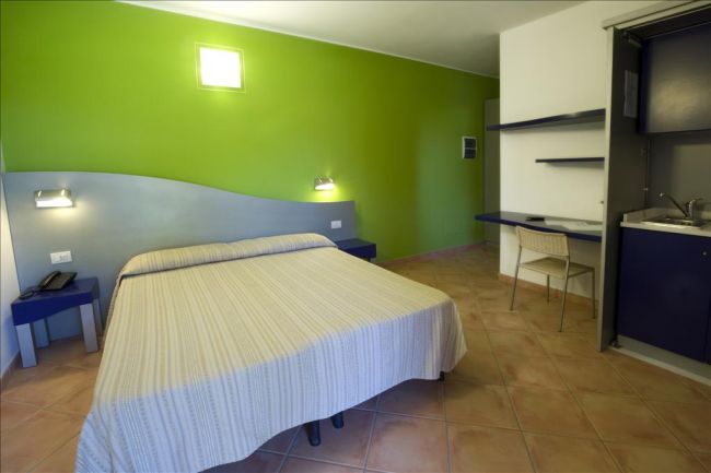 Camera con letto matrimoniale, pareti verde e bianca, con scrivania e sedie.