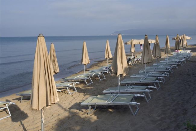 Spiaggia con lettini e ombrelloni chiusi allineati sulla sabbia, vista mare.