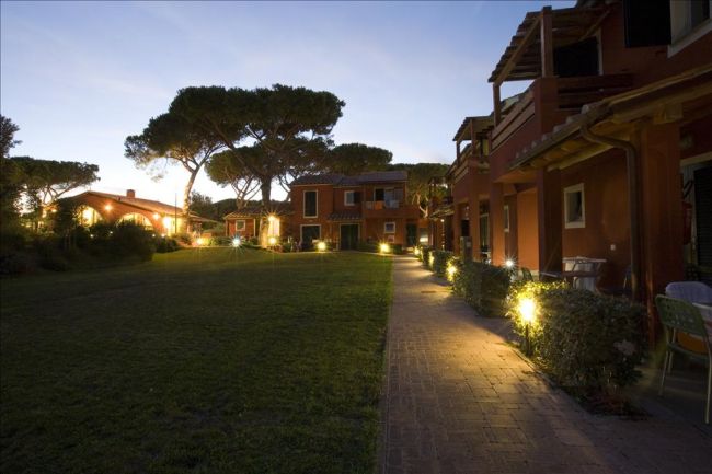 Pathway illuminato al crepuscolo tra edifici rossi e un vasto prato.