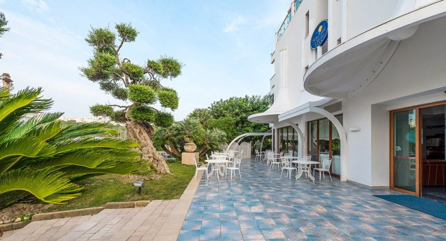 Terrazza esterna con sedie bianche e giardino.
