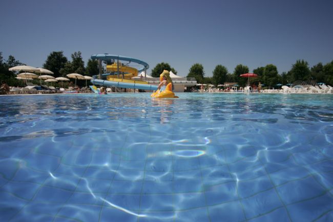Vista di una piscina con uno scivolo blu e giallo sullo sfondo. Uomo su galleggiante.
